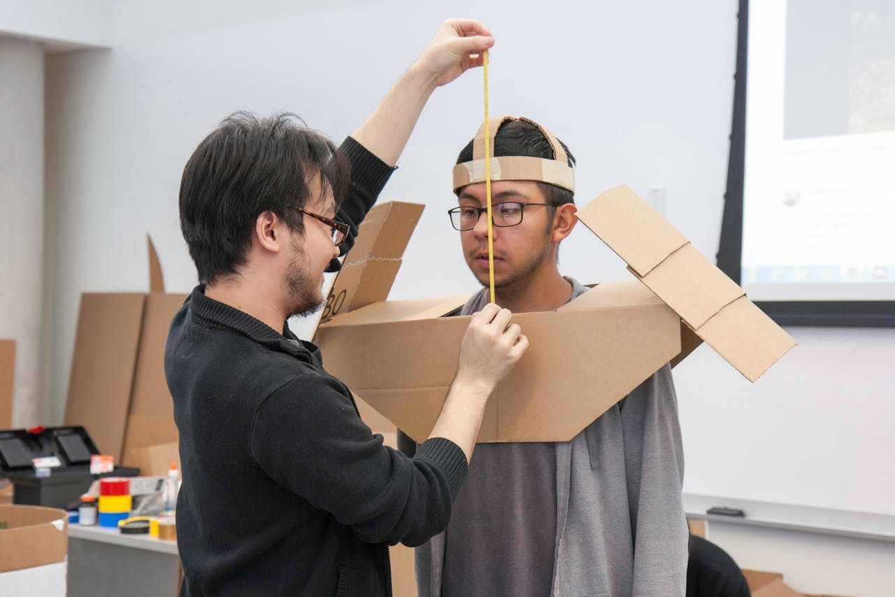 Two students collaborating on creating a cardboard costume during a classroom project activity.