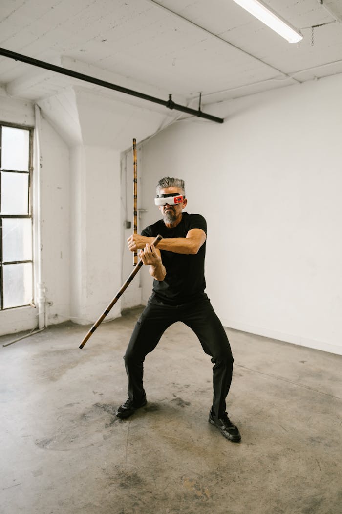 Man practicing combat skills with VR headset and stick in a minimalist indoor setting.